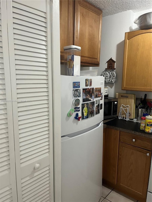 8145 NW 7th St Unit 211, Miami, FL 33126 - kitchen with freestanding refrigerator, dark countertops, light tile patterned floors, a textured ceiling, and brown cabinetry
