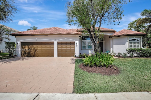 mediterranean / spanish home featuring an attached garage, stucco siding, decorative driveway, a tiled roof, and a front yard