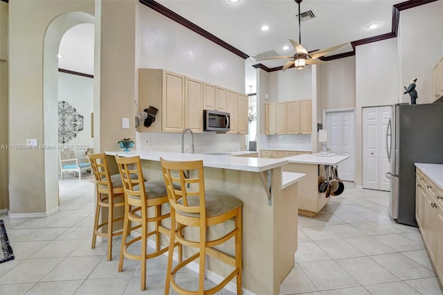 kitchen featuring appliances with stainless steel finishes, crown molding, a high ceiling, light brown cabinetry, and light tile patterned floors