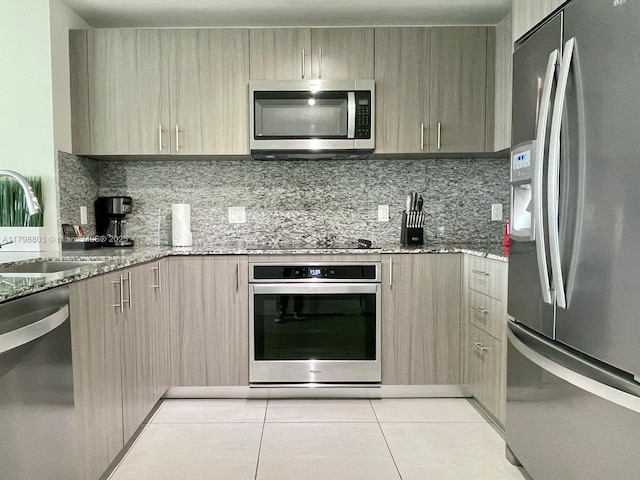 kitchen featuring appliances with stainless steel finishes, a sink, light stone countertops, and decorative backsplash