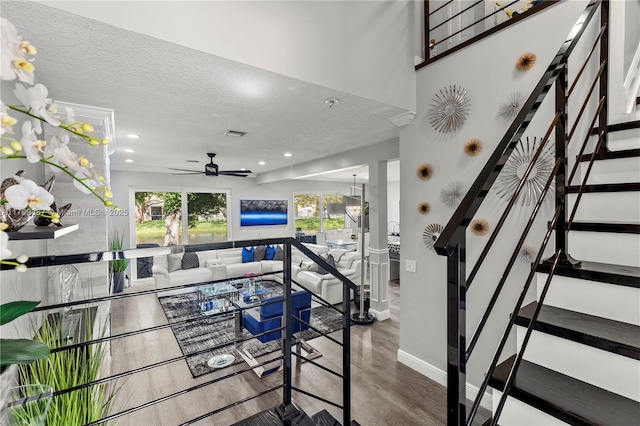 stairway featuring baseboards, wood finished floors, a ceiling fan, a textured ceiling, and recessed lighting