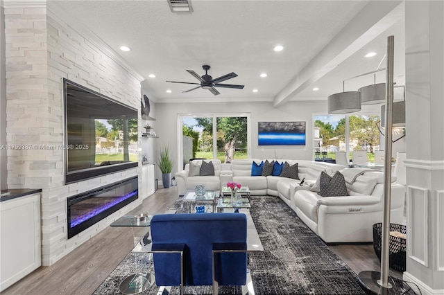 living room with a large fireplace, ceiling fan, recessed lighting, wood finished floors, and crown molding