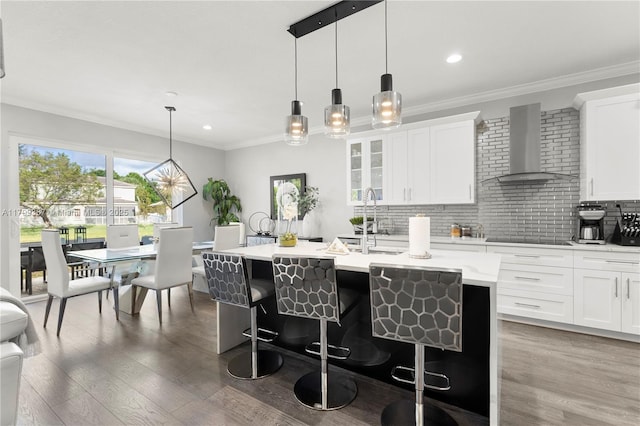 kitchen with wall chimney range hood, black electric cooktop, light countertops, a kitchen breakfast bar, and recessed lighting