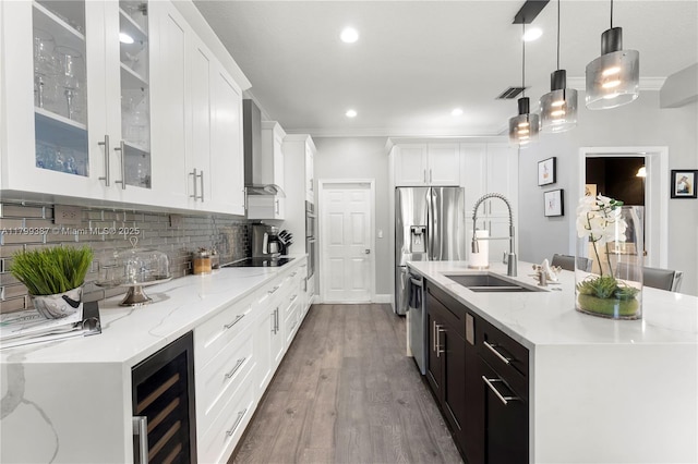 kitchen featuring a sink, wall chimney range hood, an island with sink, white cabinetry, and tasteful backsplash