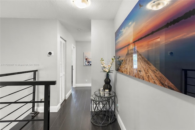 corridor featuring wood finished floors, baseboards, and a textured ceiling