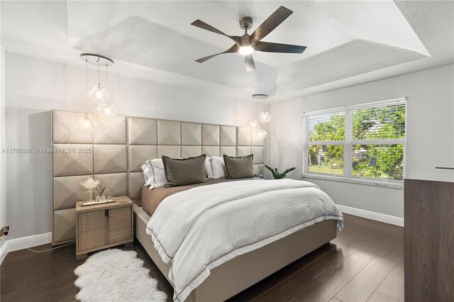 bedroom with baseboards, a tray ceiling, dark wood-style floors, and ceiling fan