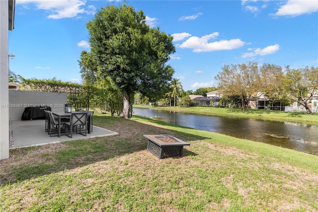 view of green lawn with an outdoor fire pit, a water view, and a patio area