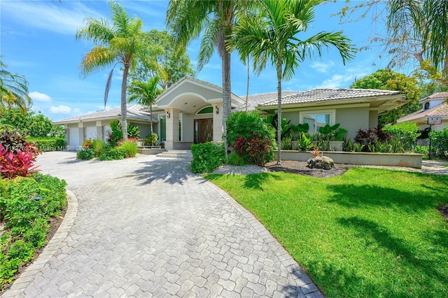 ranch-style home featuring a front yard, stucco siding, decorative driveway, an attached garage, and a tiled roof