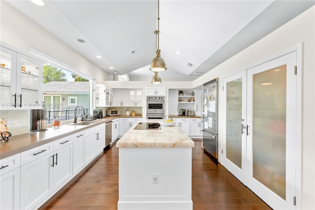 kitchen featuring open shelves, lofted ceiling, stainless steel appliances, a center island, and a sink