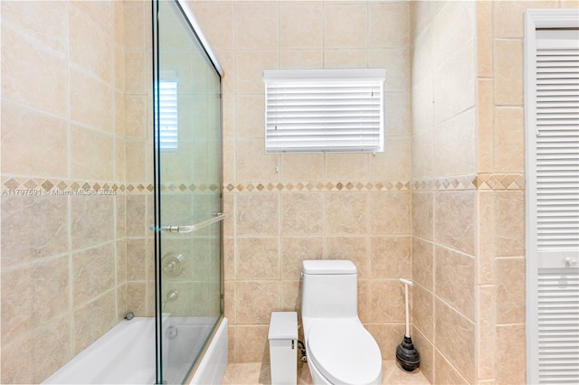 full bathroom featuring a closet, shower / bath combination with glass door, toilet, tile walls, and healthy amount of natural light