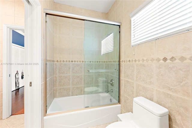 bathroom featuring tile walls, toilet, and shower / bath combination with glass door
