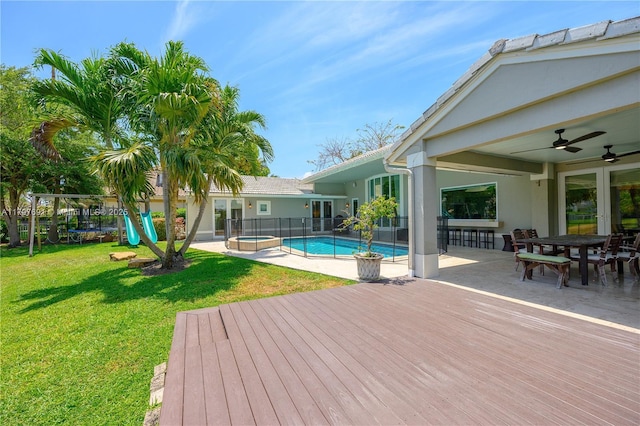 view of pool with a wooden deck, ceiling fan, outdoor dining area, a pool with connected hot tub, and a playground