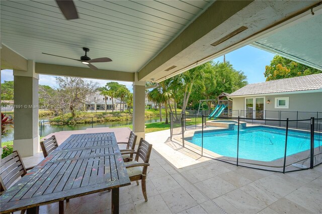 view of swimming pool with a patio area, a water view, a ceiling fan, fence, and outdoor dining space