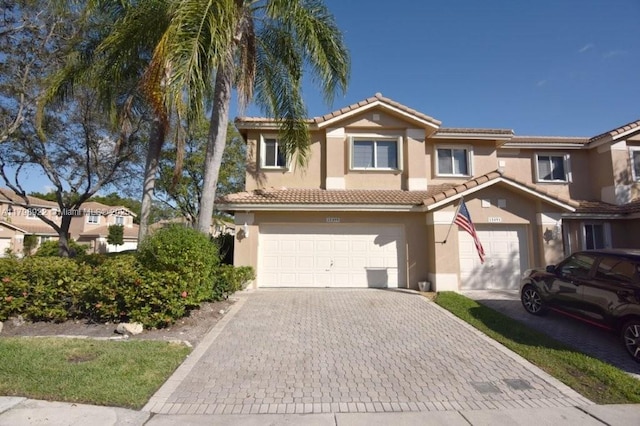 view of property featuring stucco siding, decorative driveway, a garage, and a tile roof