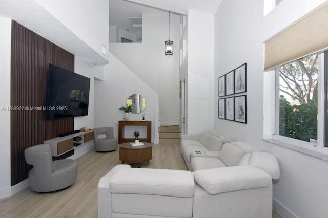 living area with a towering ceiling, light wood-type flooring, and baseboards