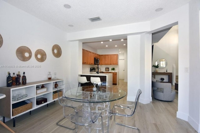 dining space featuring light wood-type flooring, baseboards, and a textured ceiling