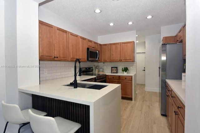 kitchen featuring stainless steel appliances, light wood-type flooring, a peninsula, brown cabinetry, and a textured ceiling