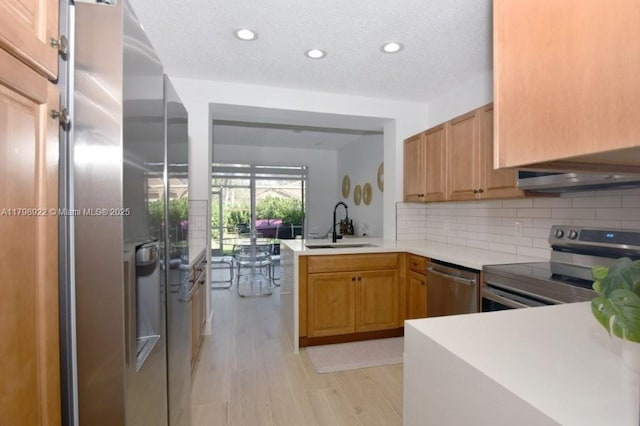 kitchen with appliances with stainless steel finishes, a sink, light wood-style flooring, a peninsula, and tasteful backsplash