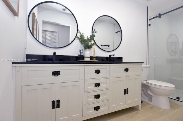 bathroom featuring a shower stall, toilet, double vanity, and wood finished floors