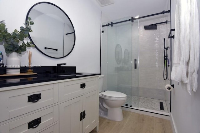 bathroom featuring wood finished floors, toilet, vanity, and a shower stall