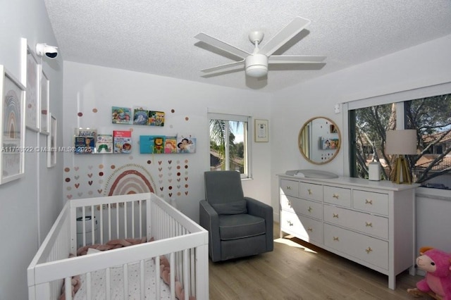 bedroom featuring wood finished floors, a crib, a textured ceiling, and ceiling fan