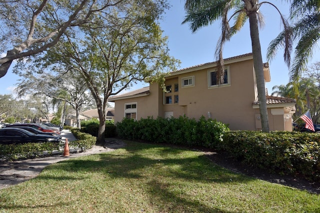 view of side of home with stucco siding, a yard, and a tile roof