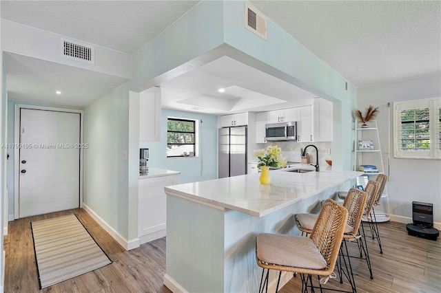 1779 NE 39th Ct Unit 1107, Pompano Beach, FL 33064 - kitchen with appliances with stainless steel finishes, a peninsula, a kitchen breakfast bar, white cabinets, and light wood-style flooring