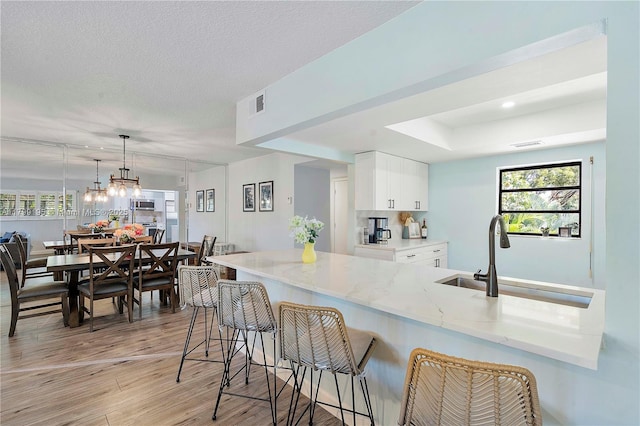1779 NE 39th Ct Unit 1107, Pompano Beach, FL 33064 - kitchen featuring a breakfast bar area, light stone countertops, a sink, light wood-style flooring, and white cabinets