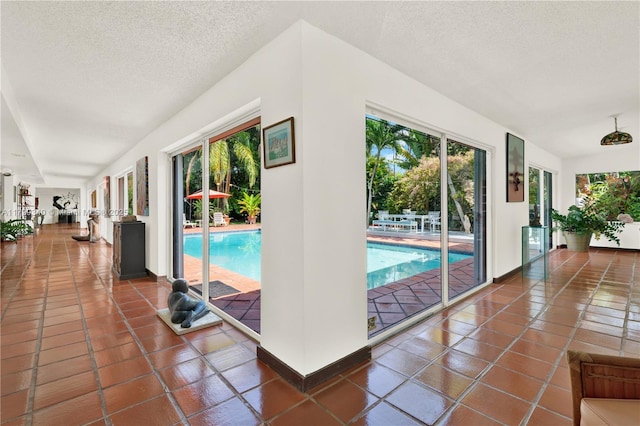 corridor featuring plenty of natural light, tile patterned flooring, a textured ceiling, and baseboards
