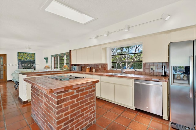 kitchen with stainless steel appliances, tile counters, a sink, and backsplash