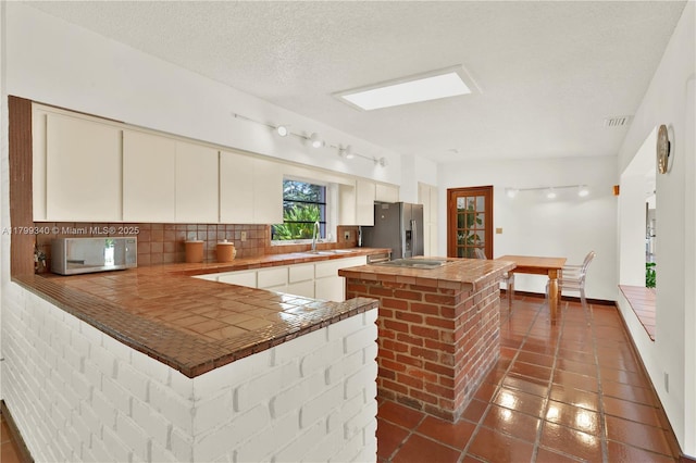 kitchen with stainless steel appliances, a sink, tasteful backsplash, tile countertops, and a center island
