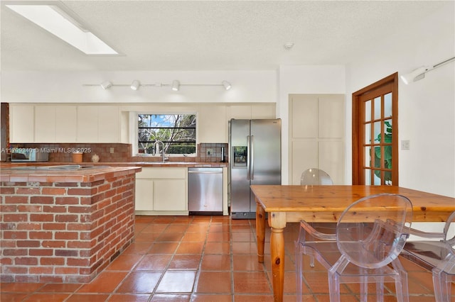 kitchen with appliances with stainless steel finishes, butcher block counters, decorative backsplash, dark tile patterned floors, and a sink