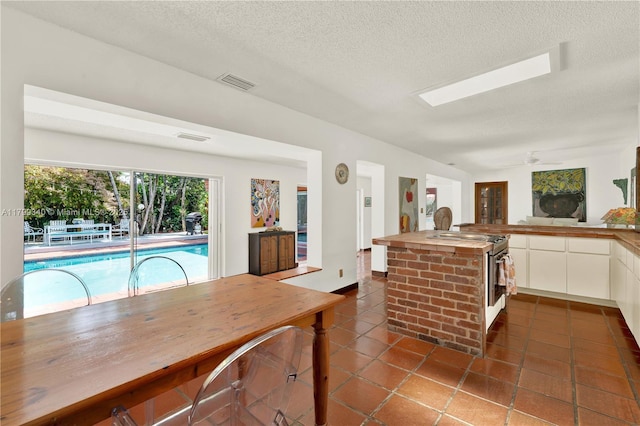 kitchen with dark tile patterned flooring, white cabinets, a textured ceiling, wood counters, and a ceiling fan