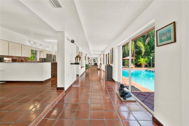 hallway with plenty of natural light, a textured ceiling, tile patterned flooring, and baseboards