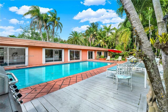 swimming pool with a wooden deck, a grill, and a patio