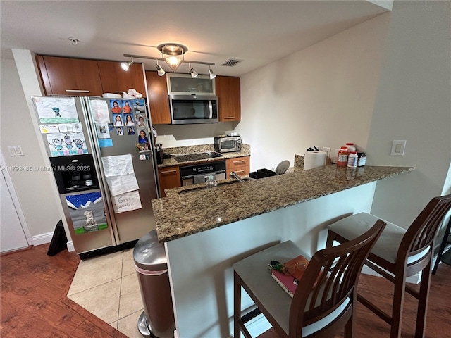 kitchen featuring black appliances, a kitchen breakfast bar, a peninsula, light wood finished floors, and dark stone counters