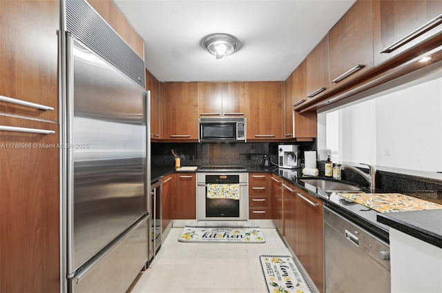 kitchen featuring appliances with stainless steel finishes, a sink, dark countertops, decorative backsplash, and brown cabinets