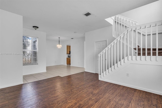 unfurnished living room featuring wood finished floors, stairway, a chandelier, and baseboards