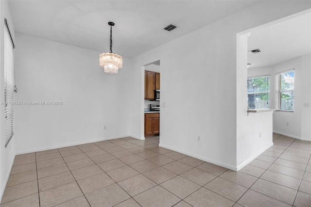 spare room with a chandelier, light tile patterned floors, and baseboards