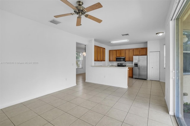 kitchen featuring appliances with stainless steel finishes, brown cabinets, light countertops, a peninsula, and light tile patterned floors