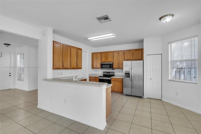 kitchen featuring appliances with stainless steel finishes, light tile patterned floors, and brown cabinetry