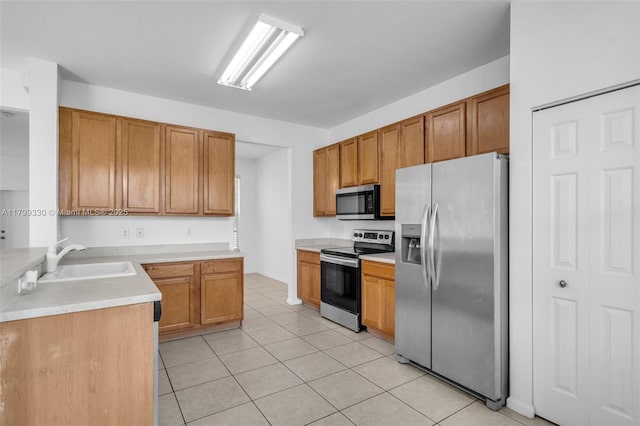 kitchen with appliances with stainless steel finishes, a sink, light tile patterned floors, light countertops, and brown cabinets