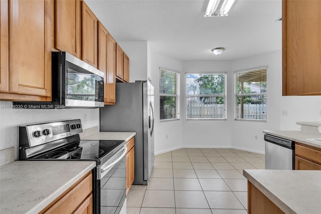 kitchen with appliances with stainless steel finishes, light countertops, light tile patterned flooring, baseboards, and brown cabinetry