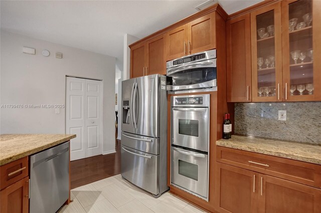 5354 NW 119th Ter, Coral Springs, FL 33076 - kitchen featuring appliances with stainless steel finishes, brown cabinetry, glass insert cabinets, and light stone countertops