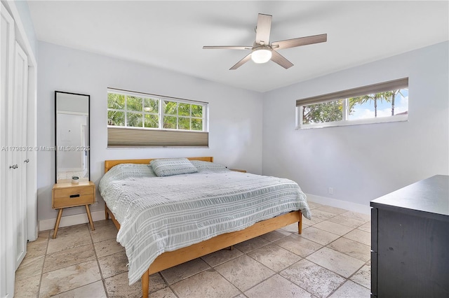 bedroom featuring baseboards, stone tile floors, and ceiling fan