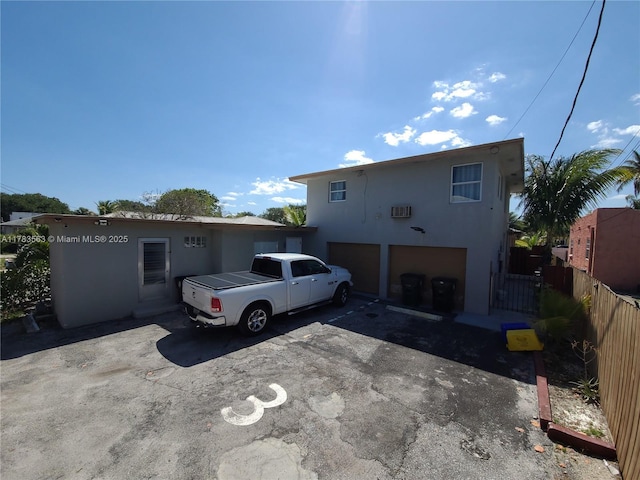 view of front facade with a garage, stucco siding, fence, and asphalt driveway