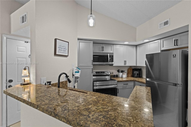 kitchen with appliances with stainless steel finishes, a sink, a textured ceiling, a peninsula, and pendant lighting