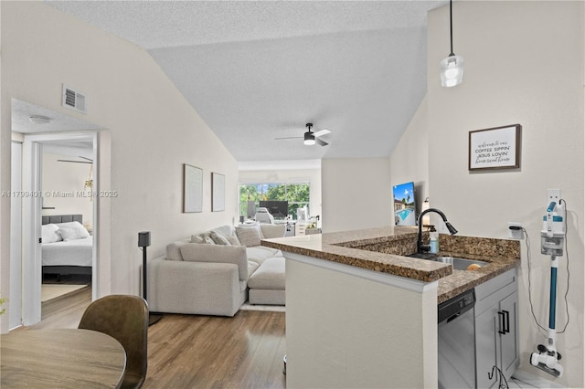 kitchen featuring lofted ceiling, a sink, dishwasher, light wood-type flooring, and dark stone counters