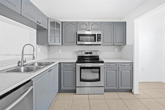 kitchen with appliances with stainless steel finishes, gray cabinetry, a sink, light tile patterned floors, and glass insert cabinets