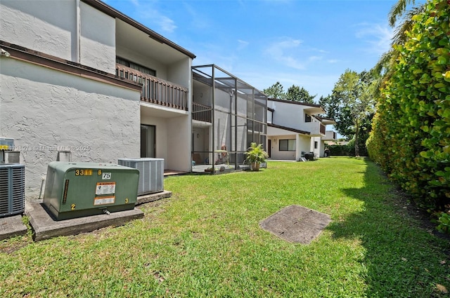 view of grassy yard with central air condition unit and a balcony